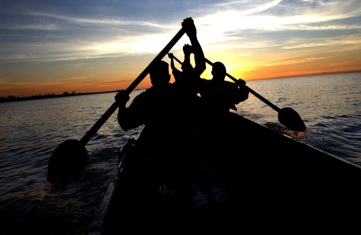 Three men are rowing, silhouetted against the setting sun