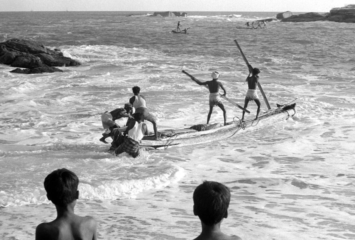 Four Indian boys row out to see as two more watch from the shore