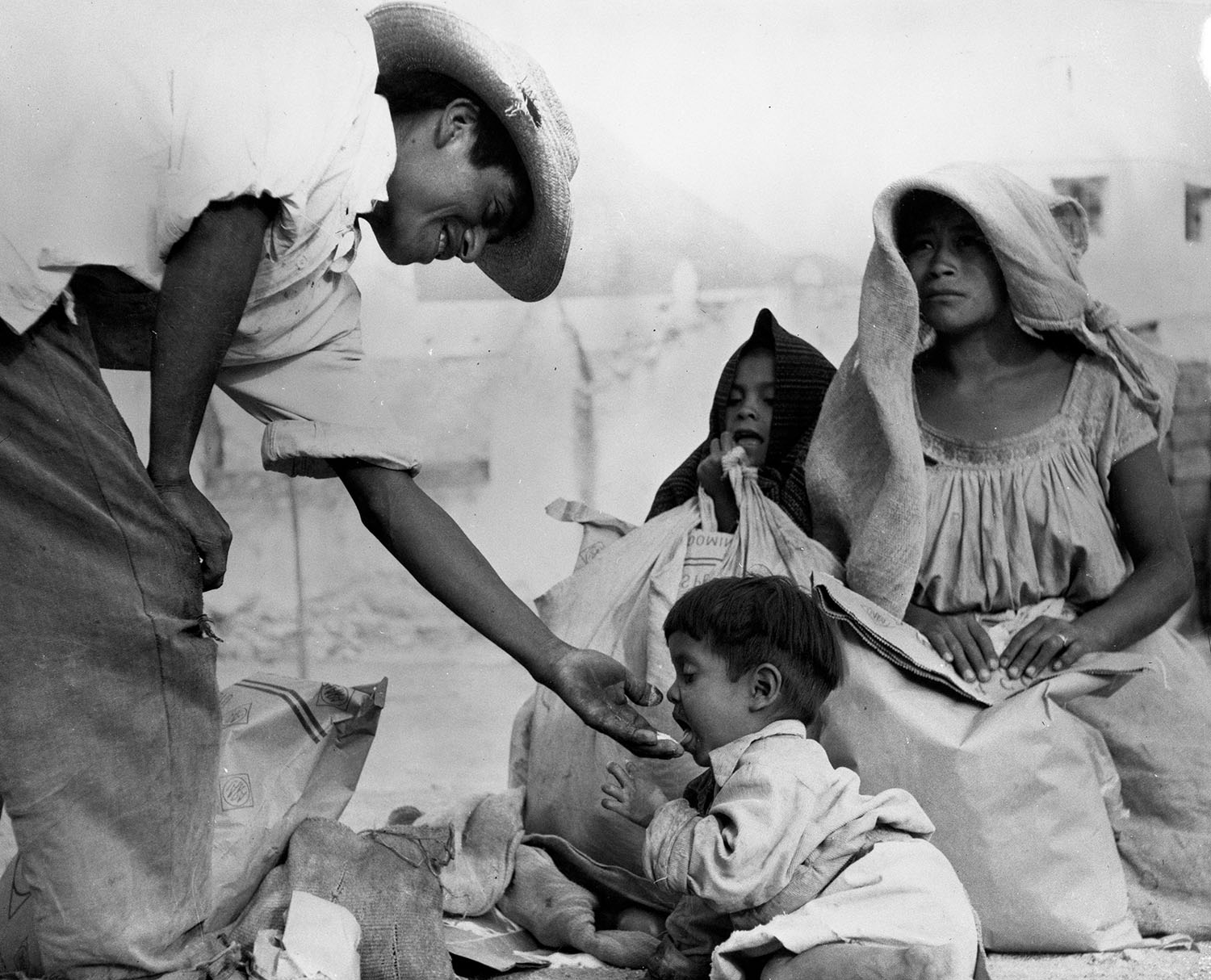 A man from Mexico's Otomi Indigenous group offers his young son a tatste of dried milk as a woman and girl watch over the scene