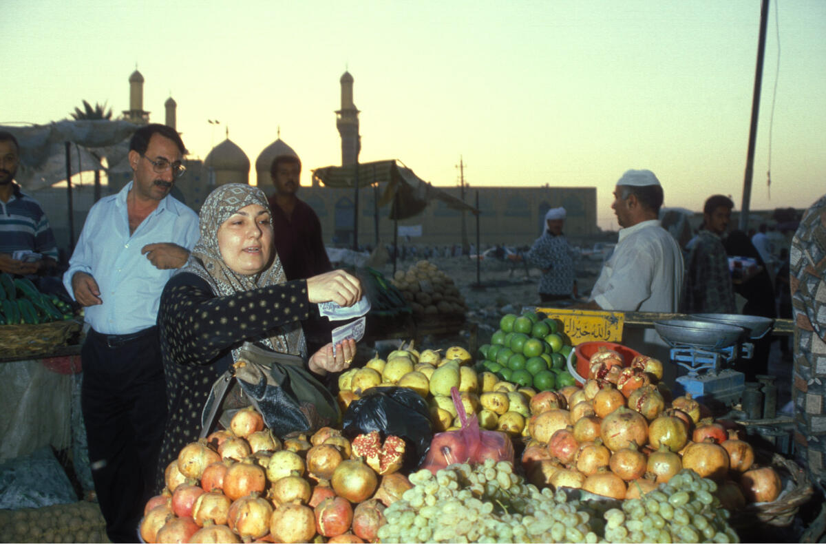 امرأة تبيع الرمان والعنب والليمون على عربة، بينما تلوح في الأفق مئذنة مسجد